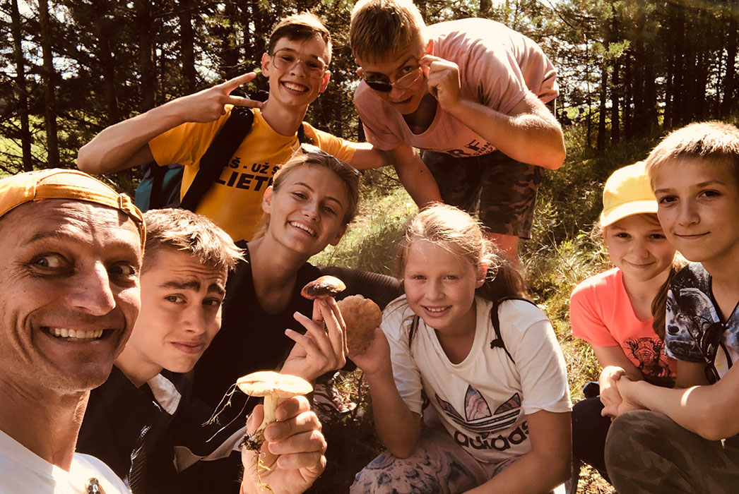 Adults and children in nature, smiling, some with mushrooms.