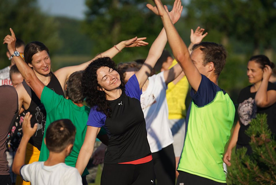 Many people in the sun, smiling and one arm stretched up towards the sky.