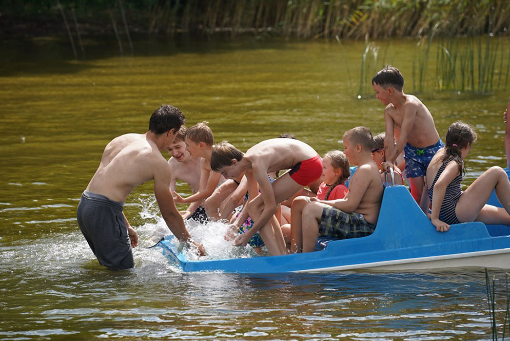 Boys and girls in a boat, laughing, splashing water.