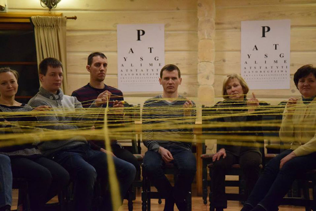 Sitting in a circle indoors, strings going across from each person, to many people